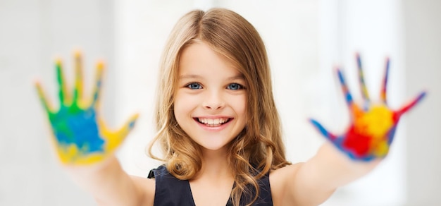 education, school, art and painitng concept - little student girl showing painted hands at school