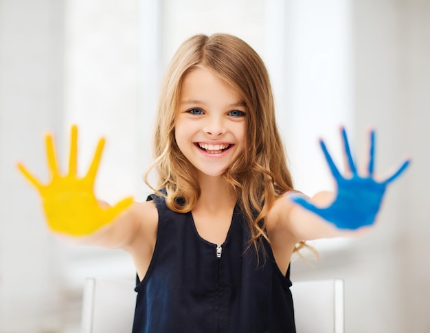 education, school, art and painitng concept - little student girl showing painted hands at school