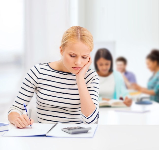 education, school and business concept - worried woman with notebook and calculator studying in college