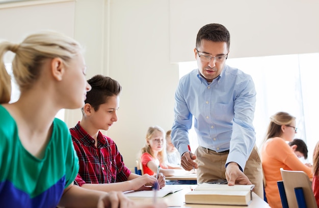 education, school, learning, teaching and people concept - group of students and teacher talking in classroom