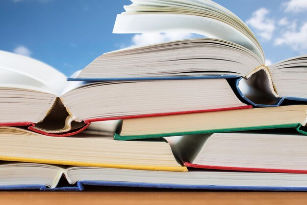 education, school, literature, reading and knowledge concept - close up of books on wooden table over blue sky and clouds background