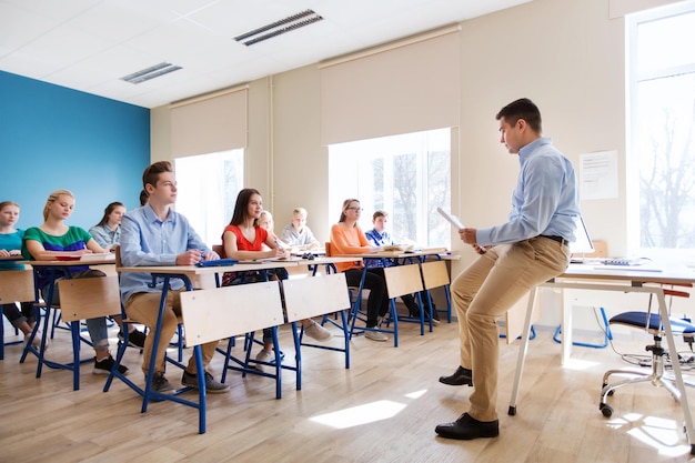 education, school and people concept - group of happy students and teacher with papers or tests