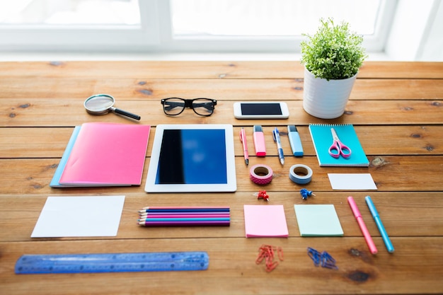 education, school supplies, art, creativity and object concept - close up of stationery and tablet pc computer with smartphone on wooden table