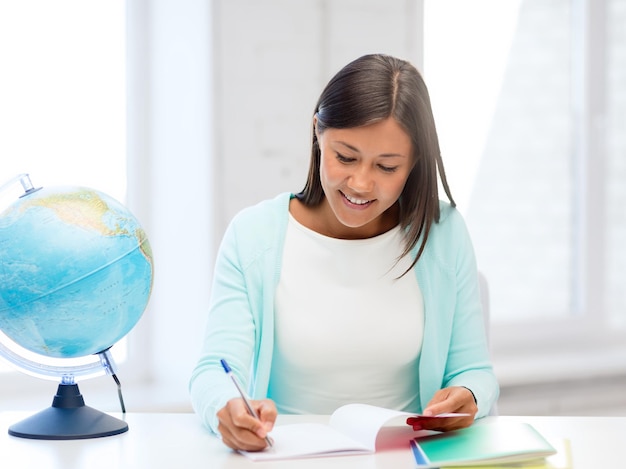 education and school, travel concept - female teacher with globe and notepad