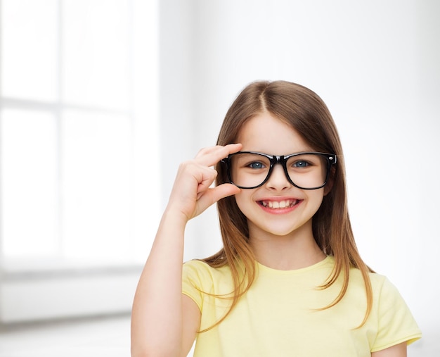 education, school and vision concept - smiling cute little girl in black eyeglasses