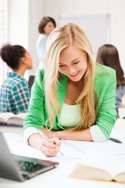 education and technology concept - smiling student girl writing in notebook at school