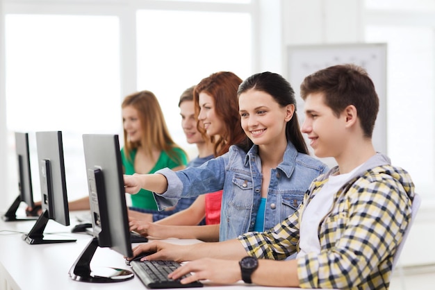 education, technology, friendship and school concept - smiling male student with classmates in computer class