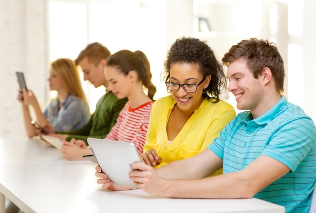 education, technology and internet concept - smiling students looking at tablet pc computer at school