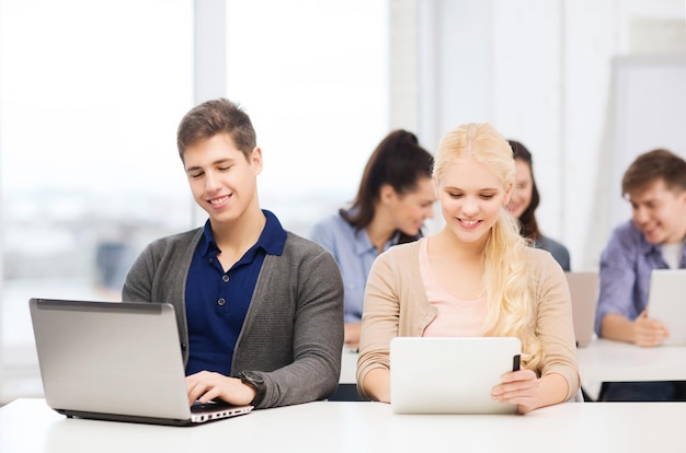 education, technology and internet concept - two smiling girl students with laptop and tablet pc at school