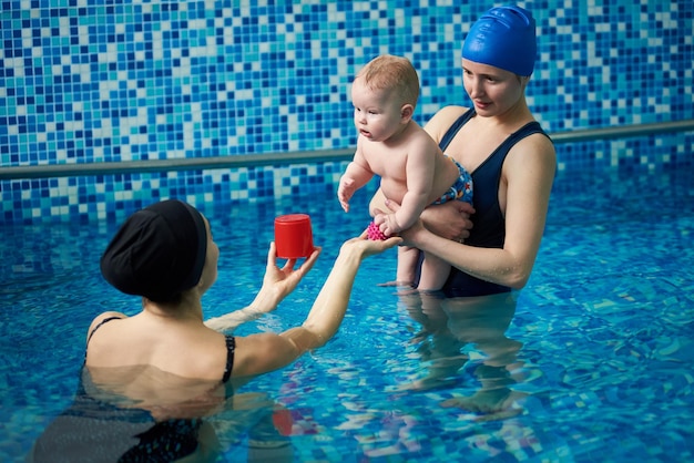 Educational games in pool with parents and specialist Cute baby boy interested in communication with swimming trainer