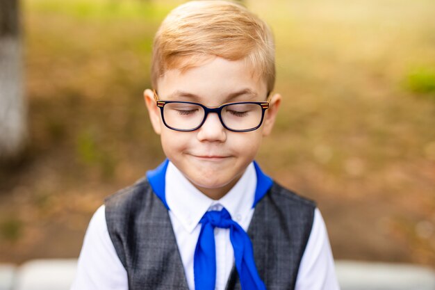 Educational theme: portrait of a schoolboy with big black glasses and blue tie. School backyard, beginning of classes