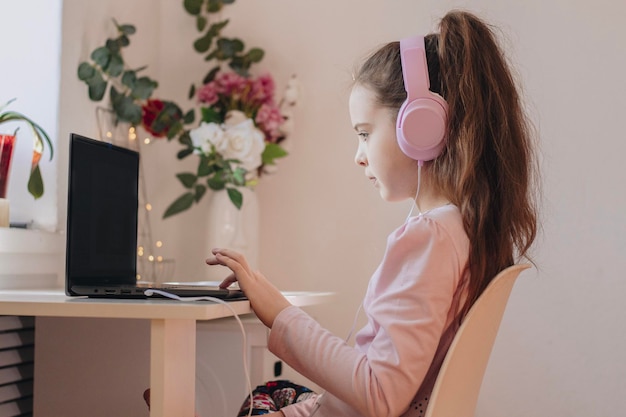 Eeducation online lessons and courses for schoolers Girl in headset looking at laptop watching online lesson or listening to tutor home interior