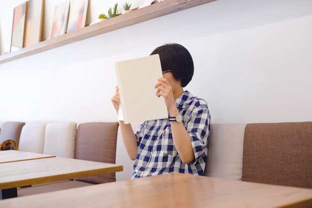 Eenage girl holding and reading blank book or magzine on sofa at cafe in lifestyle concept