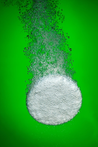 Effervescent tablet in water with bubbles on a green background