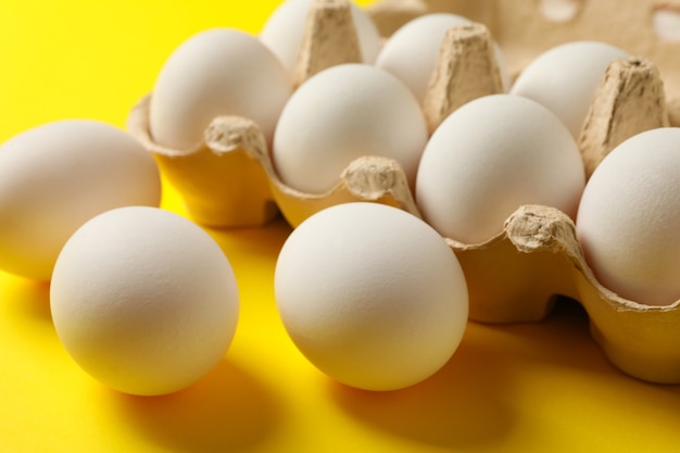 Egg box with fresh eggs on yellow background