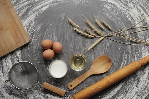 Egg, flour, olive oil, milk, wheat ears, kitchen tool on gray table