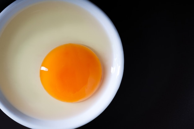 Egg yolk on a white plate on black background with space for copy