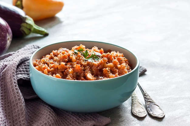 Eggplant caviar in blue bowl and fresh vegetables on background. Copy space