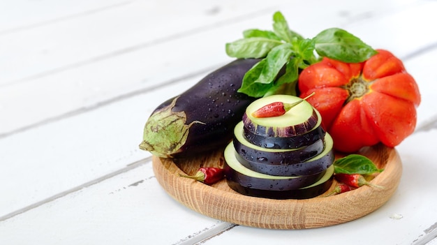 Eggplant tomato and fresh basil on a wooden plate on a white background with copy space Ingredients for the eggplant dish