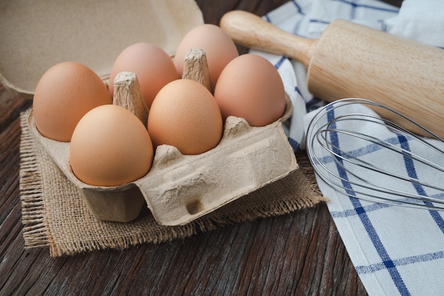 Eggs in carton with whisk and rolling pin on wooden table for cook and bakery concept