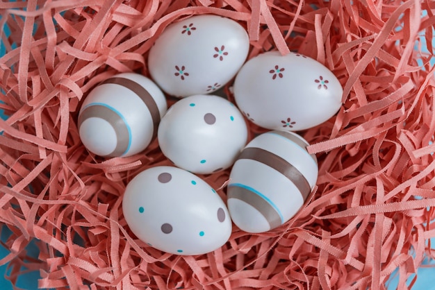 Eggs decorated with stripes, dots and flowers in coral nest on blue table, Easter concept.