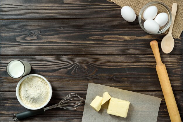 Eggs, flour, butter, whisk and milk on a wooden table. Home cooking.