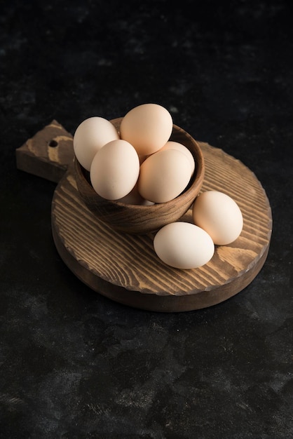 Eggs on wood board in wooden bowl dark background