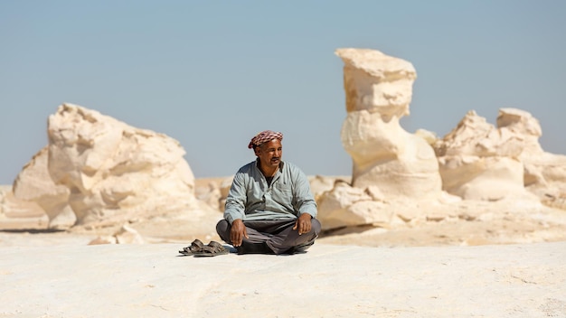 An Egyptian sits near sandstone formations in the Black and White Desert. Egypt.