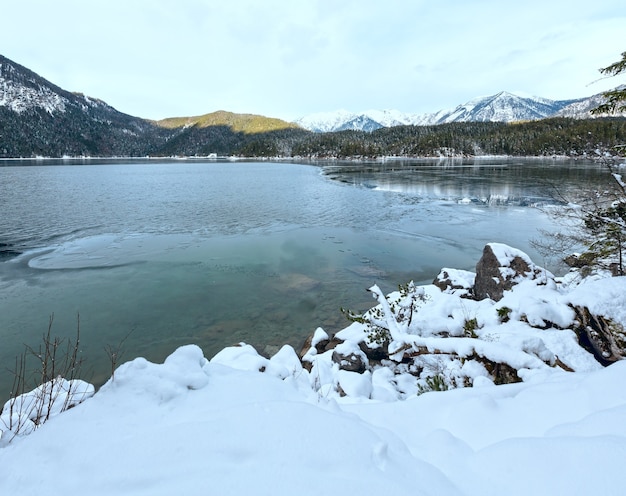 Eibsee lake winter view with thin layer of ice on the surface and snowdrift, Bavaria, Germany.