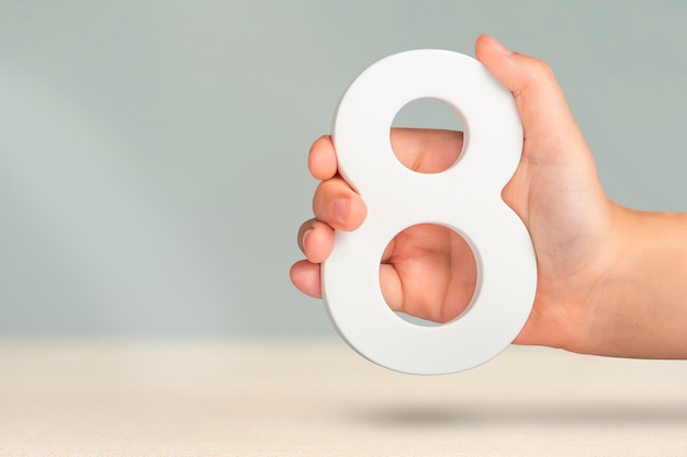 Eight in hand A hand holds a white number 8 on a blurred background Concept with number eight Birthday 8 years percentage eighth grade or day international women's day