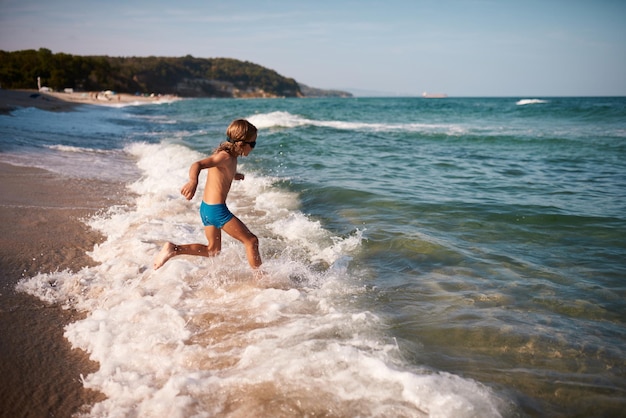 Eight year old boy with long blond hair joyfully runs to swim in the sea