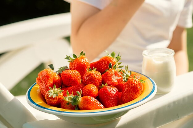 Photo an eightyearold boy eats strawberries with yogurt in the summer in the yard