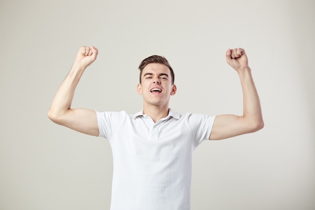 Elated guy dressed in a white t-shirt and jeans is on a white background in the studio .