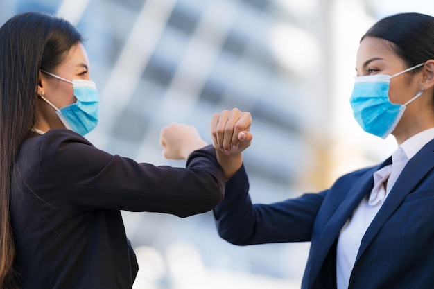 Elbow bumping, New normal, Female colleagues wearing protective face masks greeting bumping elbows