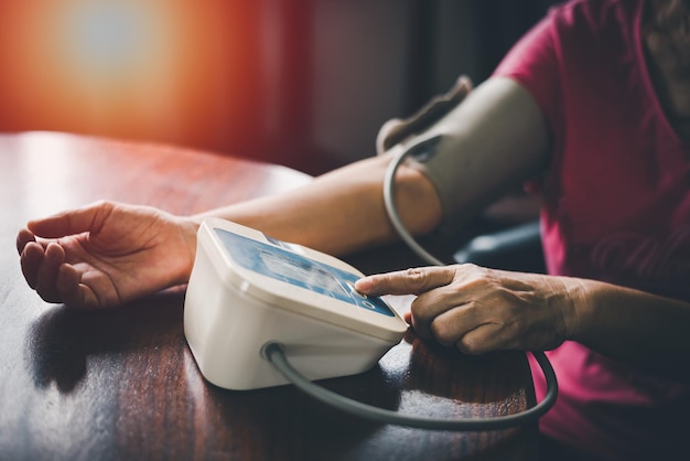 Elder woman upper arm bicep in cuff Older retired lady measuring manually blood pressure using digital tonometer machine at home Healthcare disease treatment concept