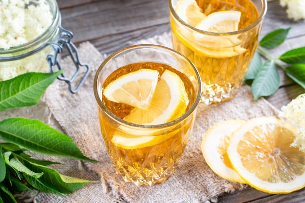 Elderberry flowers and lemon drink. Refreshing healthy summer juice. Glass of elderflower lemonade on wooden rustic board. Alternative medicine and therapy.