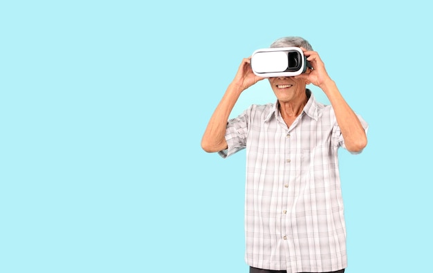 Elderly Asian man playing VR video game with virtual reality goggles blue background in studio