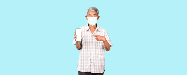 Elderly Asian man wearing a mask is sick Pointing finger holding mobile phone on blue background