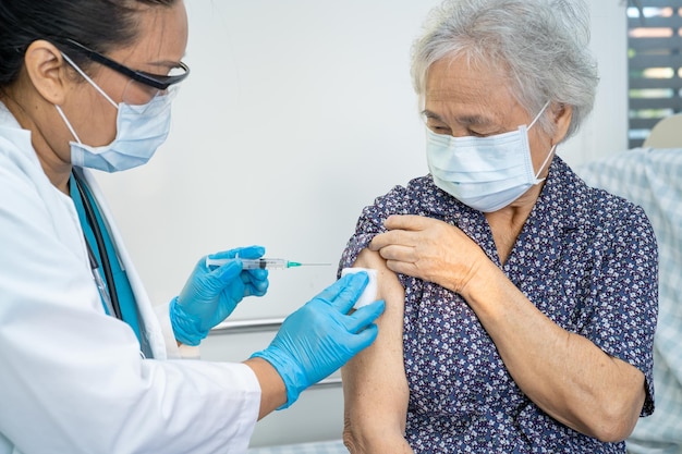 Elderly Asian senior woman wearing face mask getting covid-19 or coronavirus vaccine by doctor make injection.