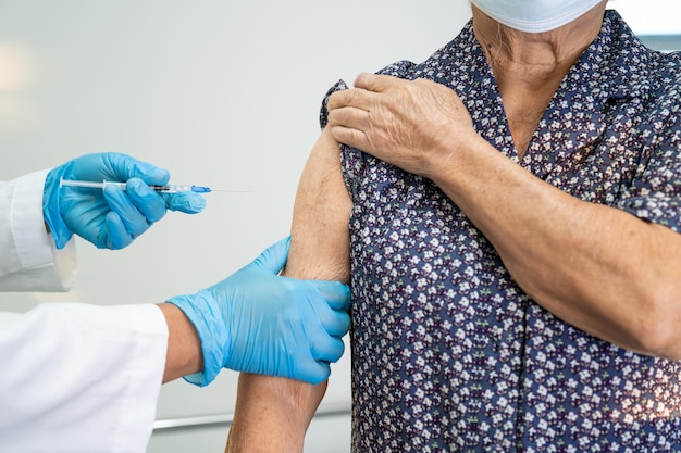 Elderly Asian senior woman wearing face mask getting covid-19 or coronavirus vaccine by doctor make injection.