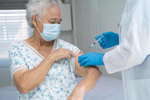 Elderly Asian senior woman wearing face mask getting covid 19 or coronavirus vaccine by doctor make injection