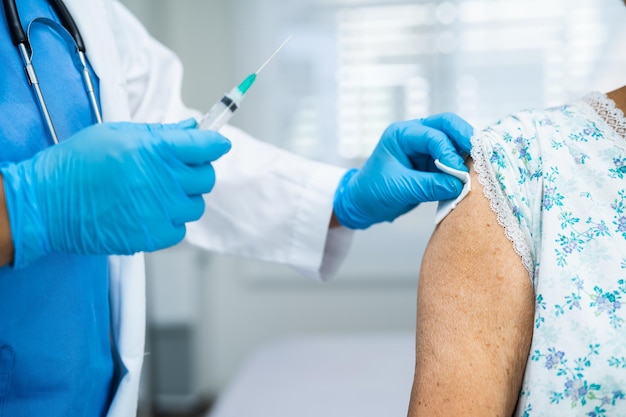 Elderly Asian senior woman wearing face mask getting covid19 or coronavirus vaccine by doctor make injection