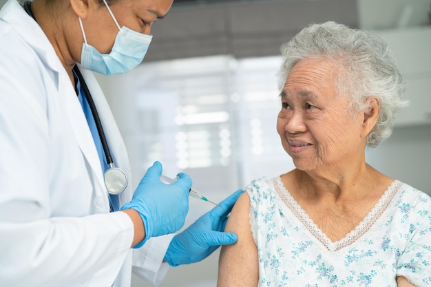 Elderly Asian woman wearing face mask getting covid19 or coronavirus vaccine by doctor make injection