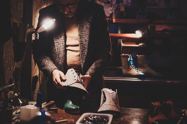 Elderly boots maker is working on his new shoe collection at workshop.