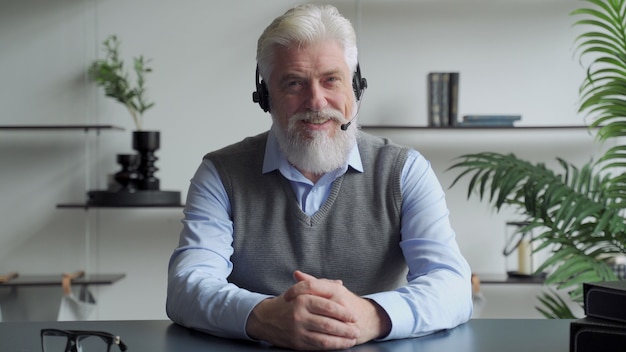 An elderly businessman in a headset having a video conference with a business partner working in an office