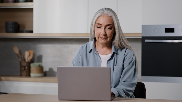 Elderly businesswoman female senior freelancer work on laptop from home typing on laptop keyboard