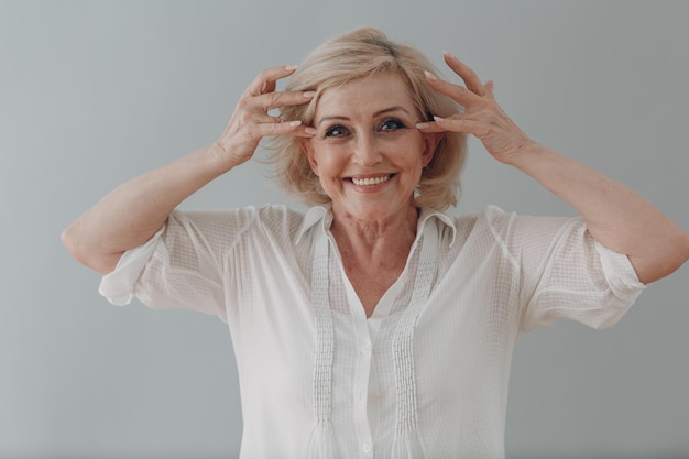 Elderly caucasian old aged woman gray haired portrait doing facebuilding yoga face gymnastics yoga self massage.