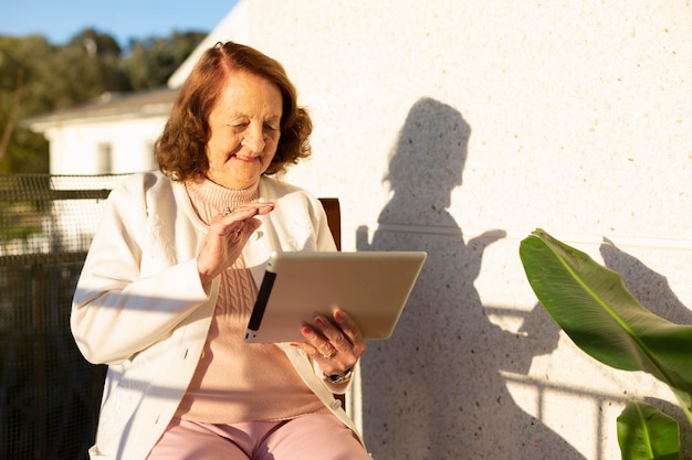 Elderly Caucasian woman making a video call from a digital tablet on the terrace of her house Concept of elderly people and new technologies