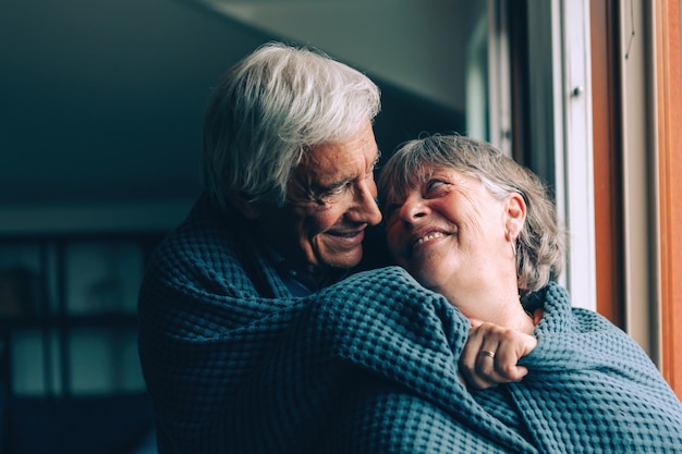 Elderly couple indoor under the blanket - senior couple relaxing at home wrapped in a blue blanket