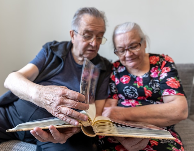 An elderly couple is looking at photographs in a family photo album.